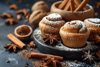 Freshly baked spiced muffins dusted with powdered sugar surrounded by cinnamon sticks, star anise, and cocoa powder on dark slate surface for bakery marketing.