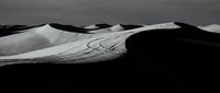 Dramatic black and white desert sand dunes with flowing curves and deep shadows creating abstract landscape composition for artistic projects.
