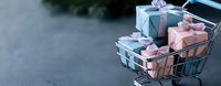 Shopping cart filled with pink and blue gift boxes tied with satin ribbons and bows on dark background, copy space for seasonal sales and holidays.