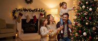 Family celebrating holidays together decorating Christmas tree with ornaments and lights in cozy living room with fireplace and garland for seasonal greeting cards and festive marketing.