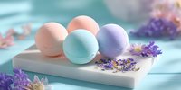 Colorful bath bombs in pastel peach, mint, and lavender arranged on white marble tray with scattered dried flowers on turquoise background.