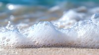 Gentle ocean foam and bubbles in macro photography showing white sea surf texture against blurred turquoise water background, natural coastal scene.