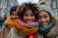 Three diverse young women wearing colorful winter accessories smile warmly at camera. Perfect for lifestyle, fashion, friendship and seasonal advertising campaigns.
