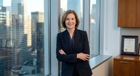 Confident mature Caucasian businesswoman in dark suit standing with crossed arms in modern corporate office with city skyline view for professional success concepts.