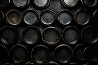 Dark vintage metal lids arranged in rows, creating industrial pattern with contrasting black and copper tones on textured background.