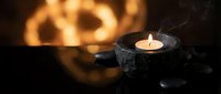 Spa candle burning in stone holder with black massage stones and warm golden light creating relaxing wellness atmosphere for meditation and aromatherapy.