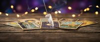 Tarot cards spread on wooden table with crystal pendulum for divination reading session with bokeh lights background creating mystical atmosphere.