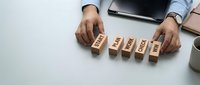 Businessman arranging wooden blocks with start, plan, work, check, win steps on white desk, showing business strategy and success concept.