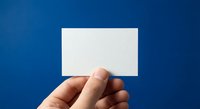 Hand holding blank white business card on blue background for mockup design and branding presentation.