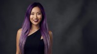 Young Asian woman with long purple hair wearing black sleeveless top smiling confidently against dark background for fashion and beauty content.