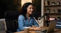 Young African American woman podcaster broadcasting live radio show in professional studio with microphone and laptop for content creation.