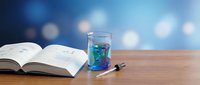 Open book with glass of blue liquid and pen on wooden desk against blurred bokeh background for study and learning concepts.