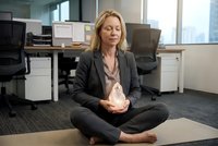 Professional blonde businesswoman meditating in modern office space, practicing mindfulness and stress relief during work break for mental health and productivity.