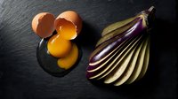 Fresh cracked eggs with golden yolks beside sliced purple eggplant on dark slate surface for culinary cooking and healthy organic food preparation.