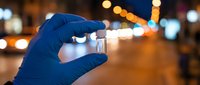 Medical professional in blue gloves holding vaccine vial at night with city lights background for healthcare and immunization campaigns.