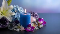 Spa wellness composition with blue candle, white lily, healing crystals, orchid flowers and smooth stones for relaxation and meditation therapy.