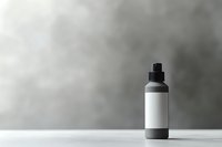 Black cosmetic bottle with blank white label on gray background, minimalist product photography for beauty and skincare packaging mockup design.