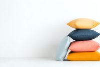 Stack of colorful cushions in pastel and bright tones against white wall, minimal home decor composition with copy space for interior design projects.