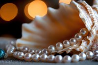 String of luminous white pearls elegantly draped over seashell with soft bokeh lights in background creating luxurious jewelry still life composition.