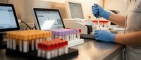 Medical laboratory technician in blue gloves analyzing blood samples with test tubes and computer equipment for diagnostic testing and research.