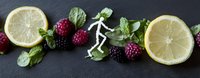 Fresh lemon slices, ripe raspberries and mint leaves arranged in line with white skeleton figure walking between fruits on dark background.