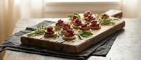 Gourmet appetizers with cranberries and herbs arranged on rustic wooden board, elegant party food presentation for holiday entertaining and catering.