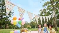 Children enjoying outdoor picnic party with colorful balloons and bunting flags in sunny park setting for summer celebration and family gatherings.