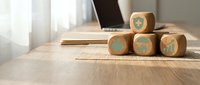 Wooden cubes with business icons on desk near laptop computer for corporate strategy planning and financial analysis presentations.