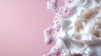 Fluffy white foam or soap suds with bubbles against pink background, macro photography showing detailed texture and soft contrast for beauty and cosmetic designs.