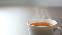 Steaming hot tea cup with aromatic vapor rising from amber liquid in white ceramic mug on neutral background for relaxation and beverage concepts.