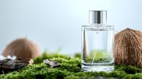 Clear glass perfume bottle with coconuts and green moss on white background for natural cosmetics and fragrance branding.