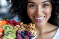 Young African American woman smiling while holding colorful bowl of fresh fruits, nuts and berries promoting healthy eating and wellness lifestyle.
