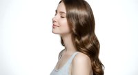 Young brunette woman with long wavy hair in profile view showing healthy shiny locks against white background for beauty and haircare concepts.