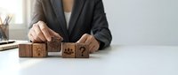Professional businesswoman arranging wooden blocks with customer service icons on white desk in modern office environment for business strategy planning.