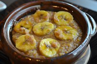 Caramelized banana slices in brown sugar sauce bubbling in ceramic pot, homemade dessert with golden syrup and melted butter creating rich caramel glaze.
