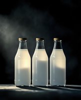 Three glass milk bottles with cork stoppers filled with fresh white milk on dark moody background with dramatic lighting for dairy product advertising.