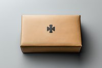 Minimalist brown leather box with embossed cross symbol on top against neutral gray background, showcasing elegant religious or spiritual packaging design.