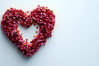 Heart shape formed by small red and pink confetti hearts on light background, romantic love symbol with negative space in center creating outline.