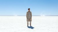 Man in casual beige cardigan standing alone on vast white salt flat under clear blue sky, suitable for minimalist lifestyle and solitude concepts.