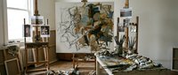Artist studio workspace with easel, paintings, brushes and creative supplies in natural sunlight for artistic projects and professional artwork creation.