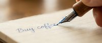 Hand writing buy coffee reminder note with fountain pen on paper close-up for shopping list planning and daily task organization.