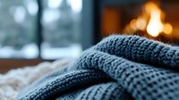 Cozy knitted wool sweater detail with fireplace and snowy window in background creates warm winter atmosphere for seasonal lifestyle and comfort concept.