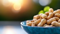 Fresh roasted peanuts in turquoise ceramic bowl against blurred natural background with golden bokeh lights and warm sunset glow.
