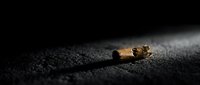 Cigarette butt on dark asphalt surface with dramatic lighting highlighting smoking waste and environmental pollution concept for health campaigns.