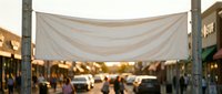 White fabric canopy stretched between wooden posts creates shade over busy outdoor market street with cars and pedestrians during golden hour sunset lighting.
