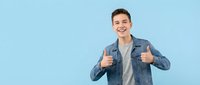 Happy young Caucasian man in denim jacket showing thumbs up gesture against light blue background. Positive attitude and approval concept for marketing.