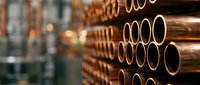 Industrial copper pipes stacked in warehouse rows with warm lighting creating depth and perspective for construction and plumbing supply concepts.