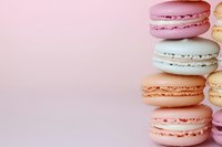 Colorful French macarons in pastel pink, peach and white arranged in vertical row on soft pink background, with copy space for text or design.