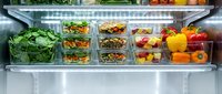 Organized refrigerator shelf displaying fresh vegetables in clear storage containers, including leafy greens, legumes, and colorful bell peppers for meal prep and healthy eating.