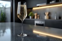 Elegant champagne flute filled with sparkling wine on modern kitchen counter with warm ambient lighting and contemporary dark cabinetry in background.